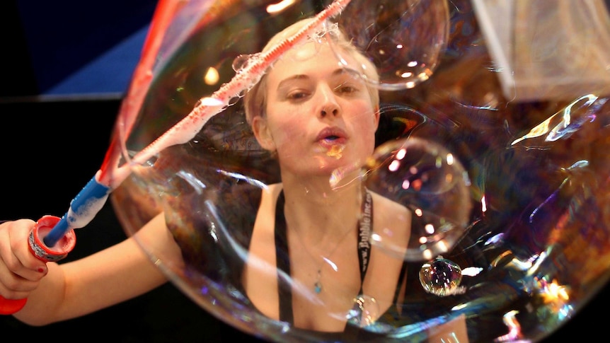 A woman entertains the crowd by blowing a large bubble at the 2013 London Toy Fair.