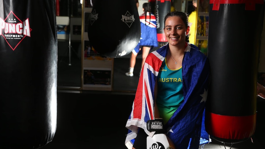 woman sits with Australian flag around shoulders in a boxing ring