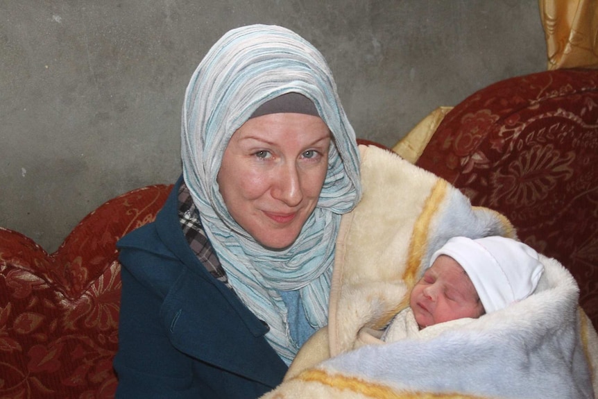 A woman in a headscarf holds a new born baby.