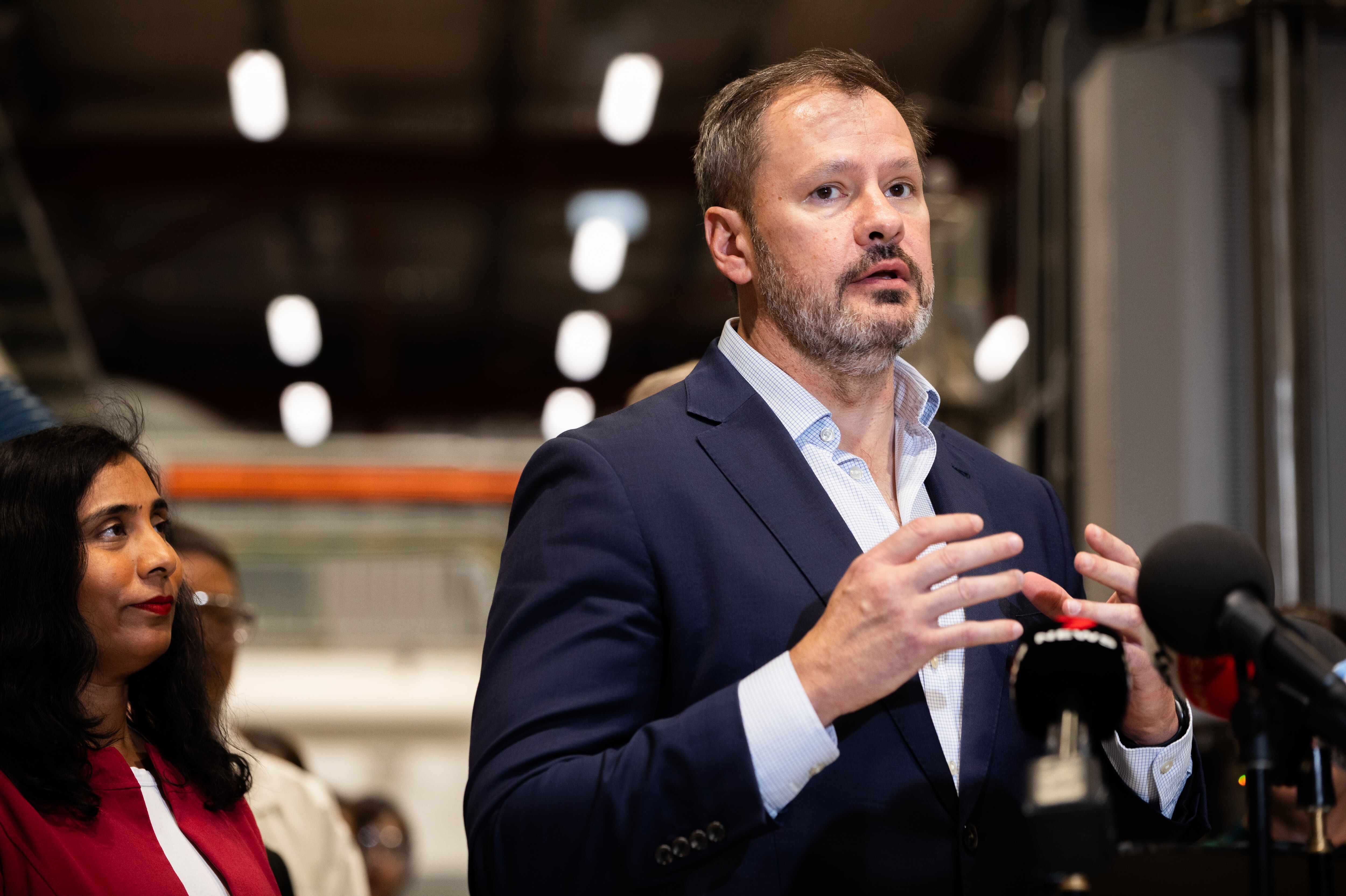 Ed Husic gestures while speaking in front of microphones.