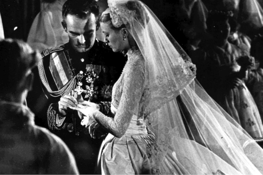 A black and white photo of a 1950s wedding, Prince Rainier of Monaco putting a wedding band on Grace Kelly's finger