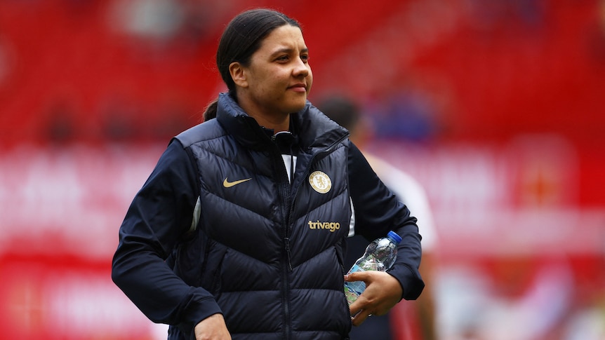 Chelsea player Sam Kerr in a jacket, holding a bottle, walking on the pitch before a match