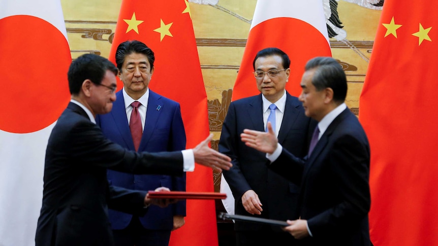 Leaders of China and Japan shake hands while in front of large flags of their respective nations