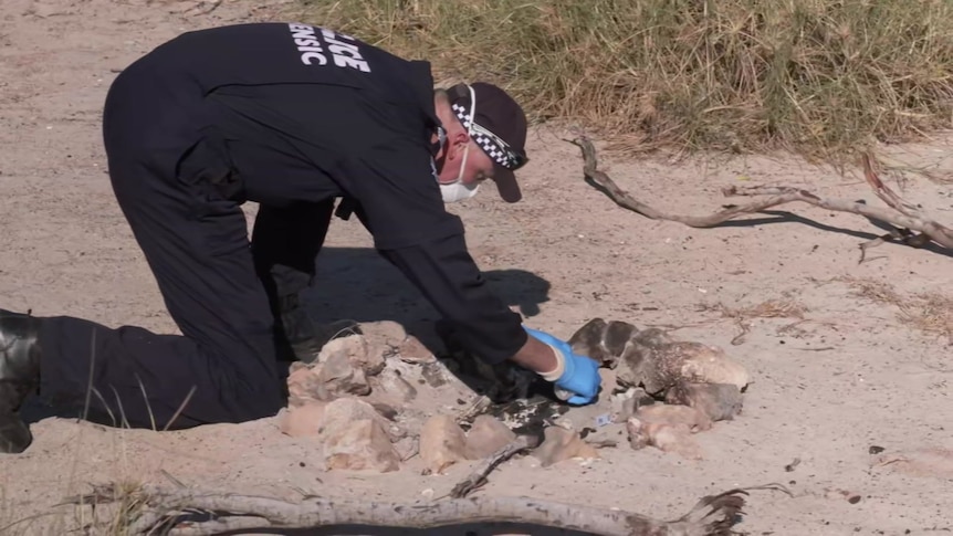 An officer sifts through ash and sand in an extinguished Blowholes campfire.