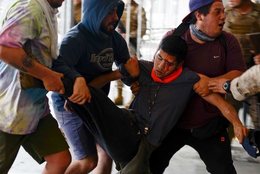 A group of protesters carry an injured man with blood streaming down his face