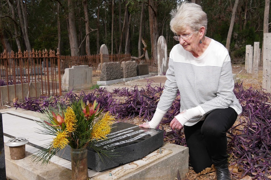 A woman sits by a grave where the headstone is laying flat.