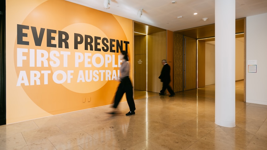 Image of person walking in front of installation, text reads "Ever Present: First Peoples Art of Australia"