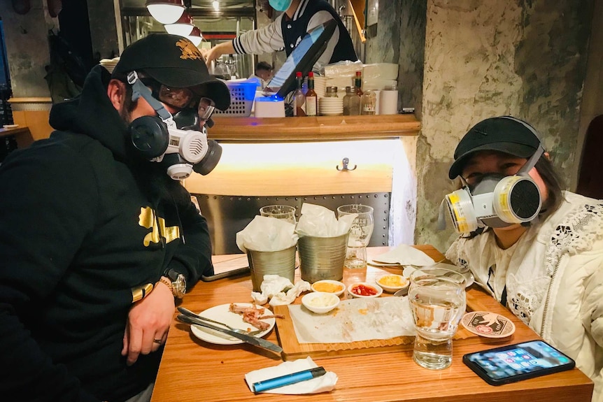 A man and woman wear gas masks as they sit at a table covered with dishes in Beijing.