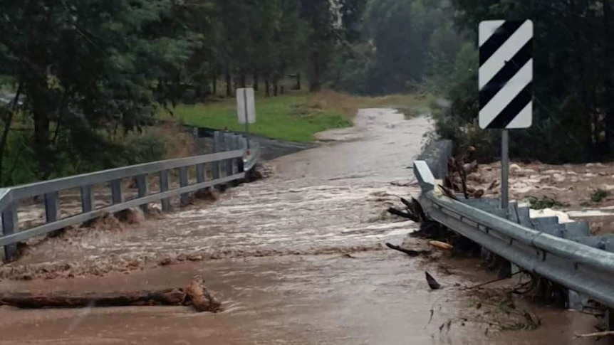 Brown flood water and a tree log cover a small country road bridge.