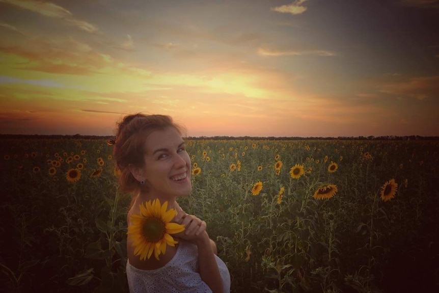 A woman smiles while standing in a field of sunflowers.