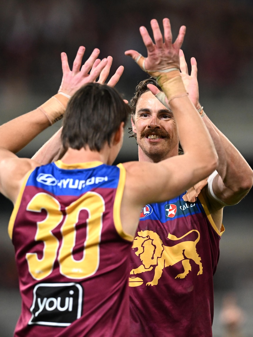 Two Brisbane Lions AFL players double high-five in celebration after a goal.