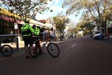 Two police officers with bicycles stand on a street with police tape