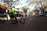 Two police officers with bicycles stand on a street with police tape