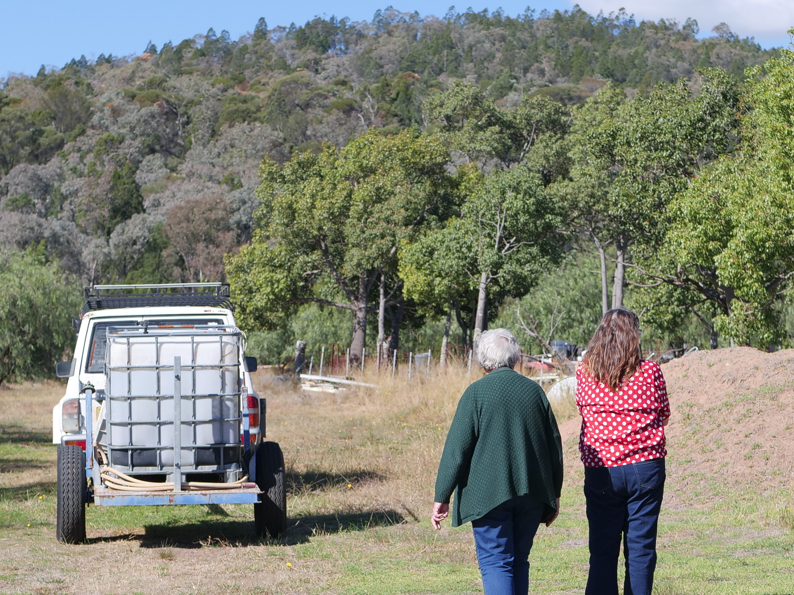 Two women walk towards an old car with sprayer on back. 
