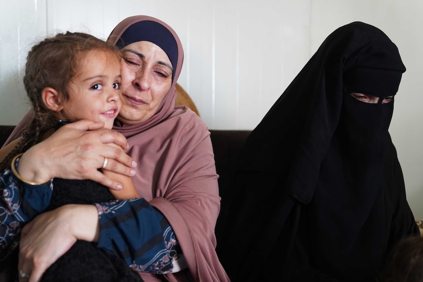 Hiam Zahab cuddles Mariam Dabboussy's child, sitting next to her daughter Nesrine Zahab in the Al-Hawl camp in Syria.