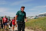Phil Mickelson walks off the course holding his scorecard being followed by a crowd of reporters