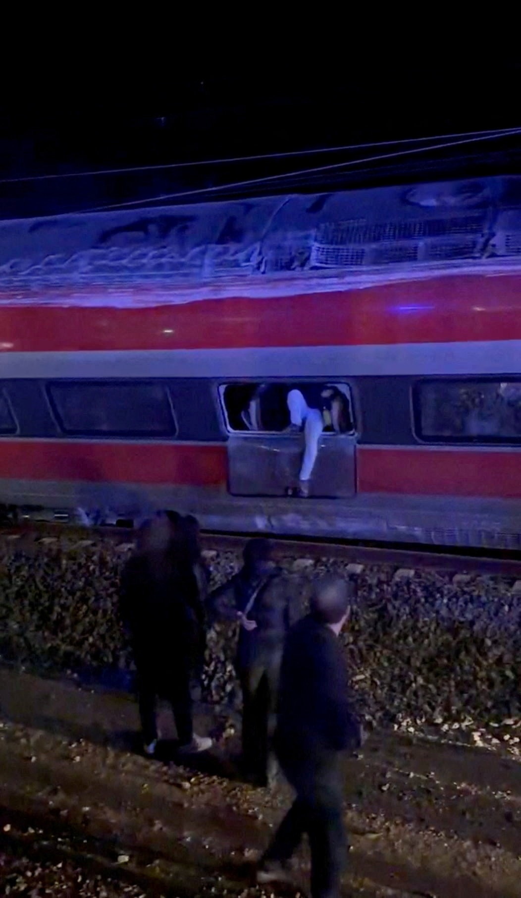 Uma pessoa é vista saindo de um dos trens descarrilados. Você só pode ver suas pernas através de uma janela. 