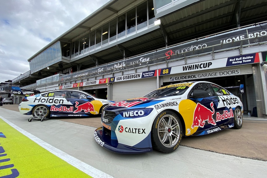 Two Red Bull Holden Commodore Supercars are parked in front of a pit garage