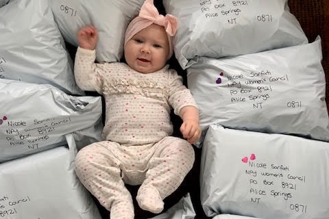 An image of baby Jedda in a pick onesie with pink bow lying on her back surrounded by grey post parcels