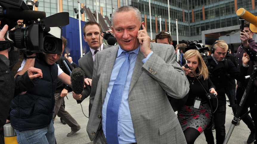 Stephen Dank talks on a mobile phone while surrounded by members of the media.