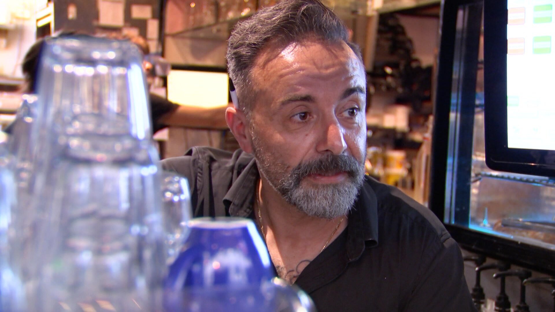 Theo Roussos standing behind the counter of his cafe with coffee cups in front of him