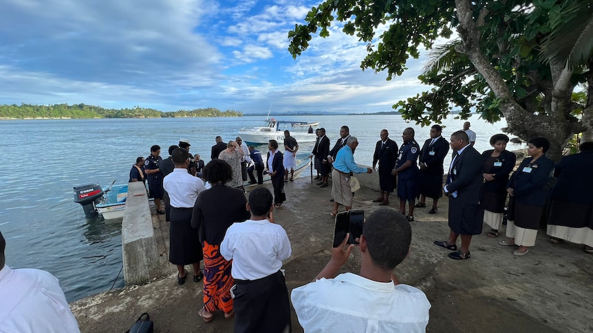 People gather at shoreline as boat comes to land.