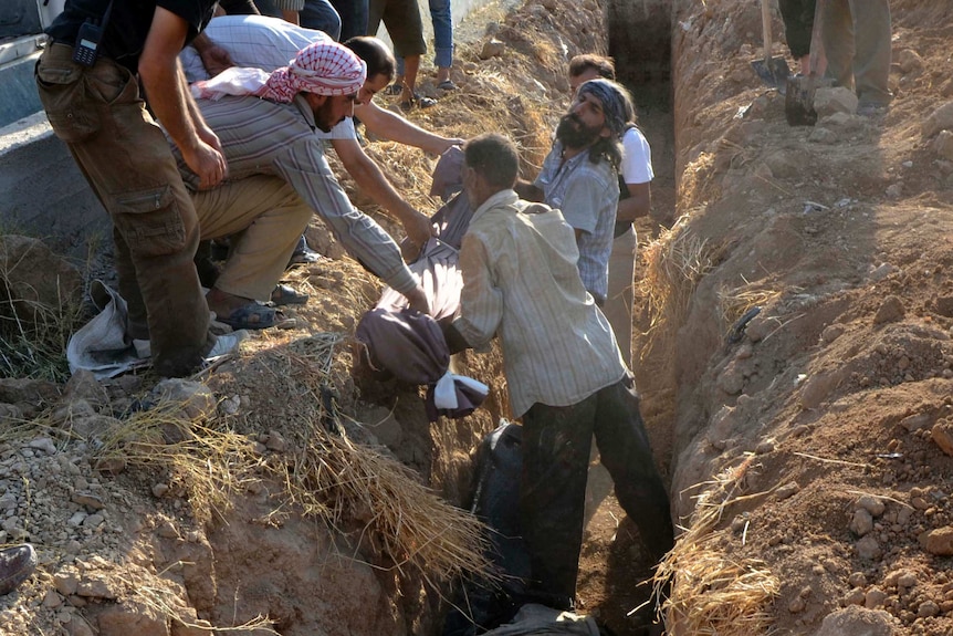 People lower a body into a grave in suburban Damascus