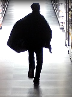 A man wearing a black cape and mask running down a supermarket aisle