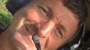 A man wearing a pilot headset smiles at the camera while sitting in a cockpit