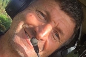 A man wearing a pilot headset smiles at the camera while sitting in a cockpit