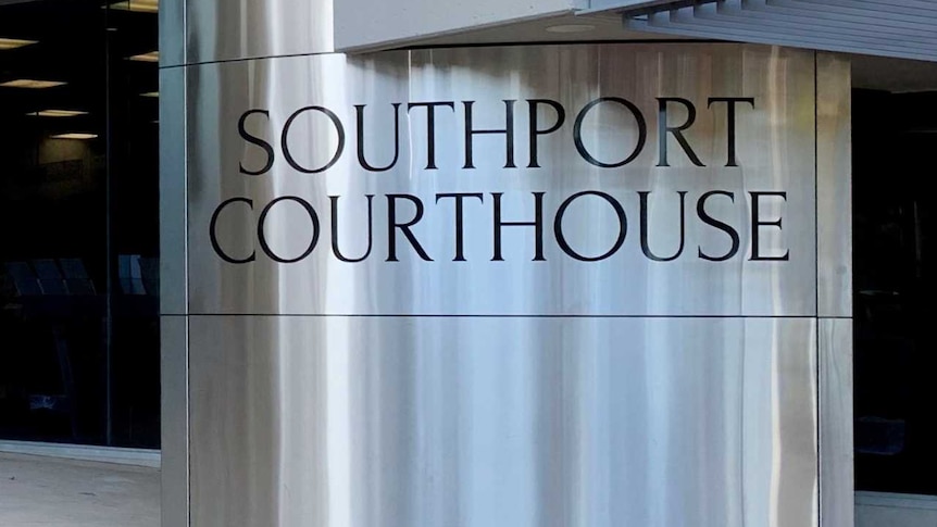 A man waits at the entry to a modern, glass and steel building with Southport Courthouse written on a shiny round pillar.