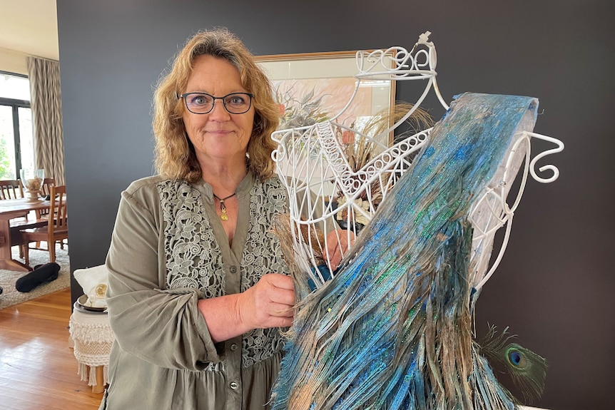 A woman stands next to a mannequin with a blue and green garment made from plant materials.