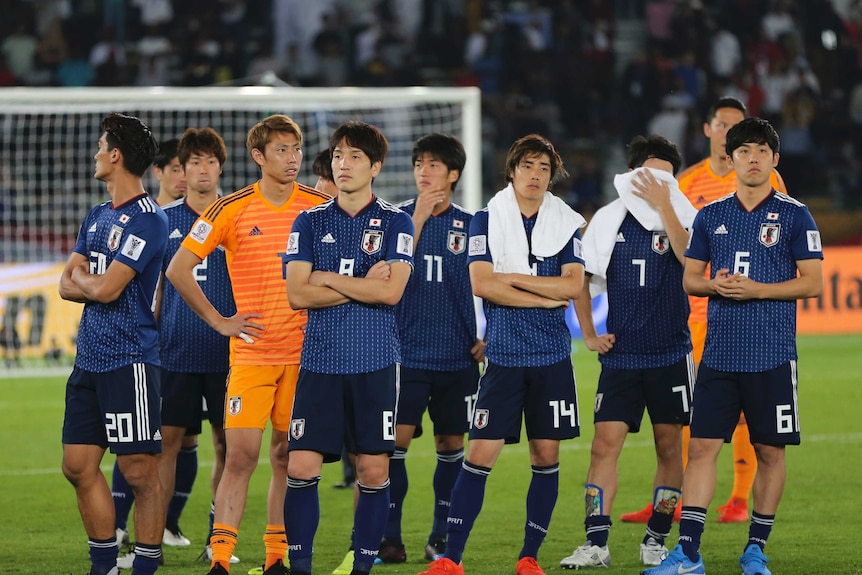 Japan players, wearing blue kit, stand in a group looking downcast after losing a final.