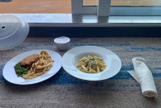 A plate of chicken schnitzel and chips sits beside a plate of pasta