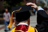A graduate holds on to his hat while talking on his mobile phone
