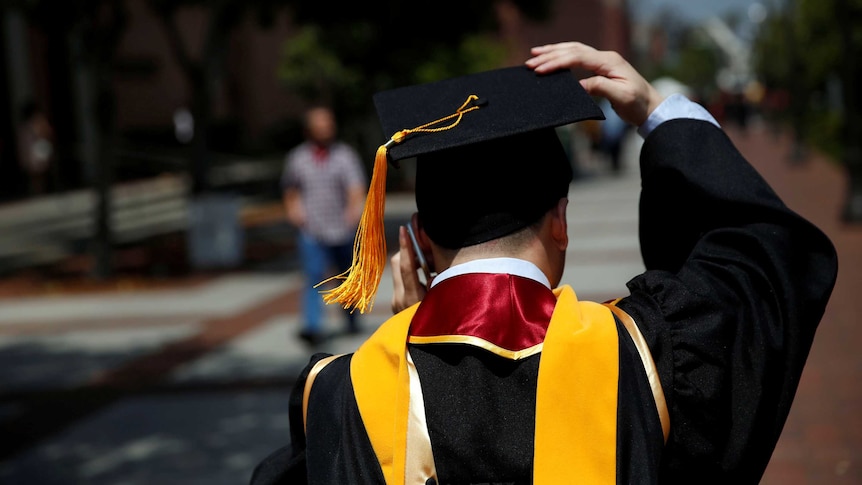 A graduate holds on to his hat while talking on his mobile phone