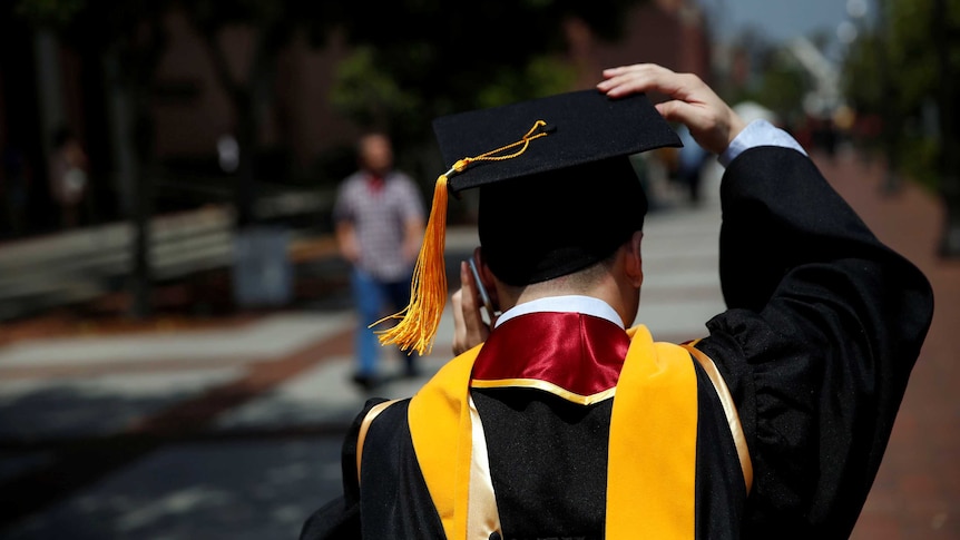 A graduate holds on to his hat while talking on his mobile phone