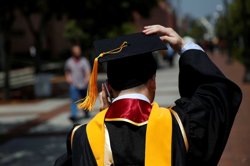 A graduate holds on to his hat while talking on his mobile phone