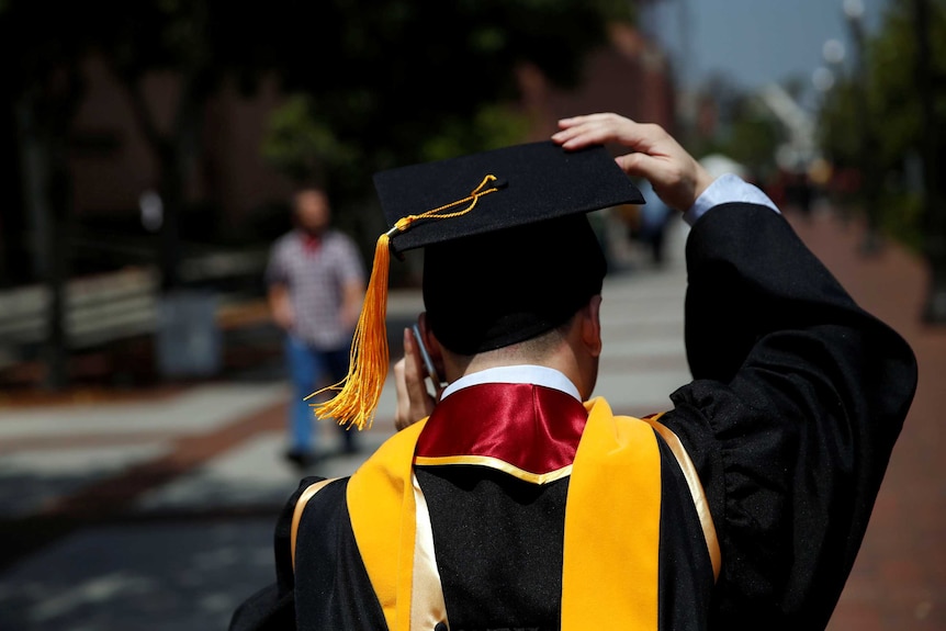 A graduate holds on to his hat while talking on his mobile phone