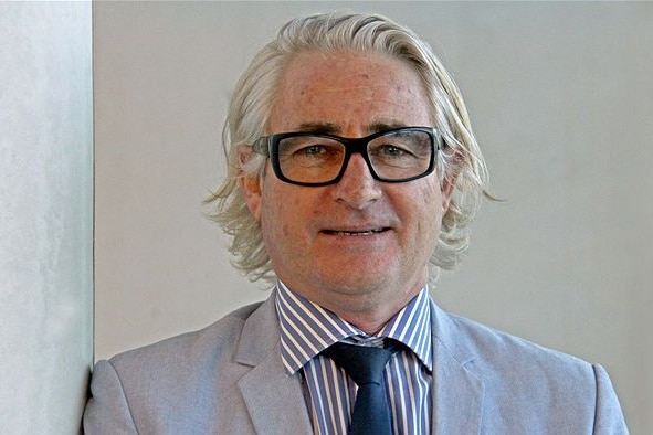 A white-=haired man in glasses and a pale suit with a pastel shirt.