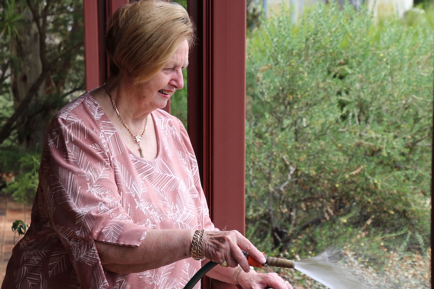 Mid shot of an older woman watering her garden.