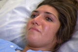 A woman cries while lying on a hospital bed.