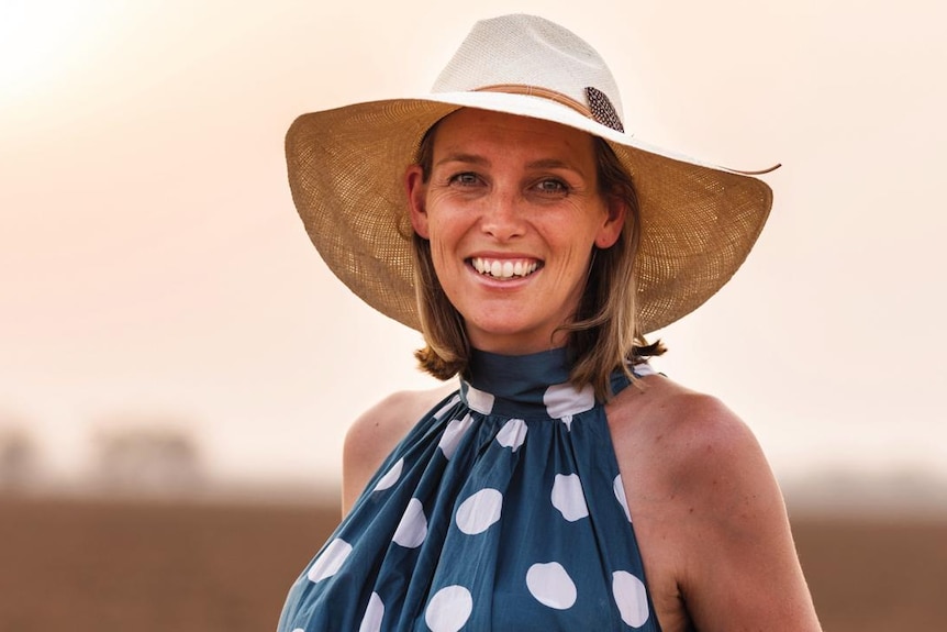 A woman wearing a hat and blue and white dress smiles.