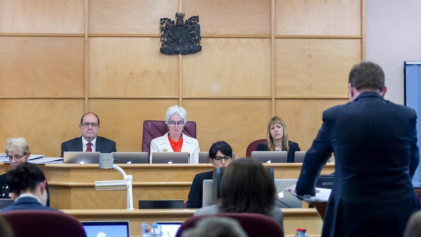 Three commissioners set at the front of a court room at the royal commission hearing.