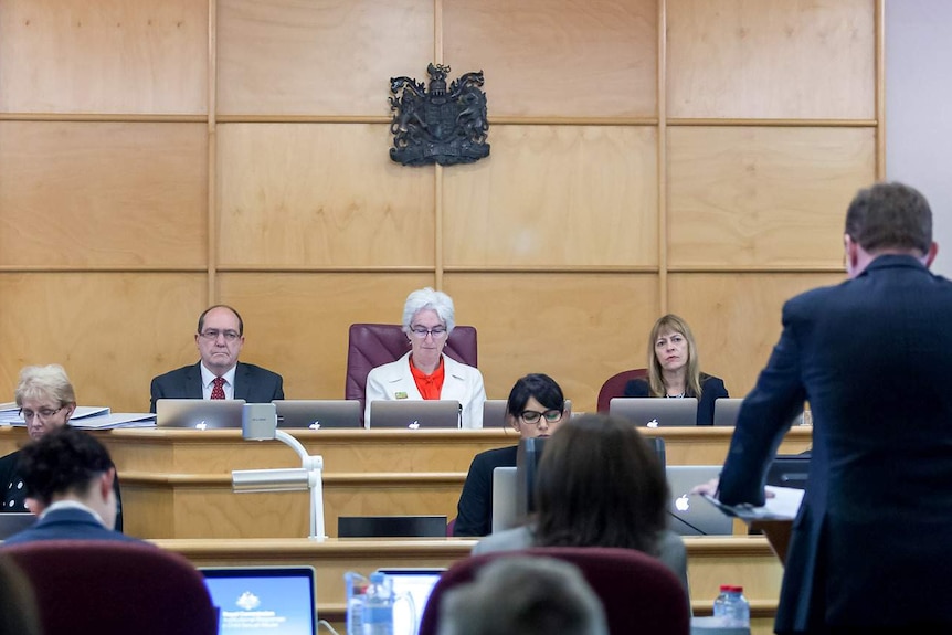 Three commissioners set at the front of a court room at the royal commission hearing.