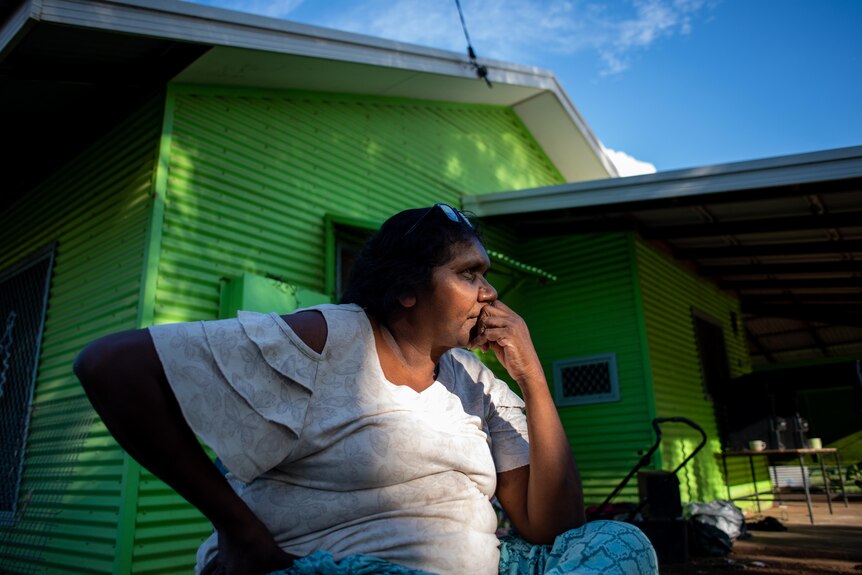 Evelyn Andrews sits barefoot outside her home.
