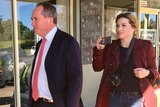 Barnaby Joyce walks in front of Vikki Campion walk past a Family First campaign poster in a shop window.