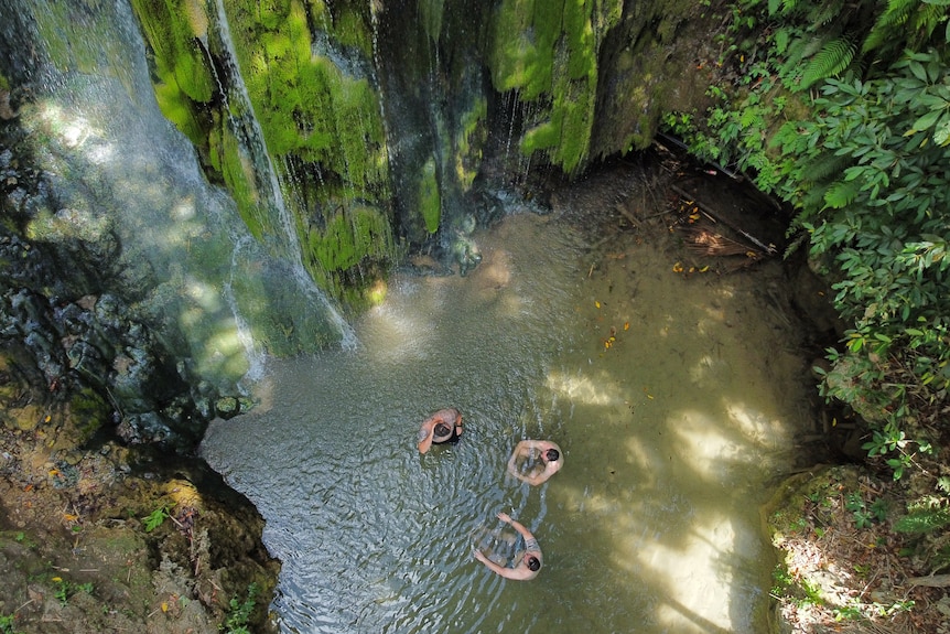 Former soldiers sit in a shallow pool near a waterfall in Timor-Leste. 