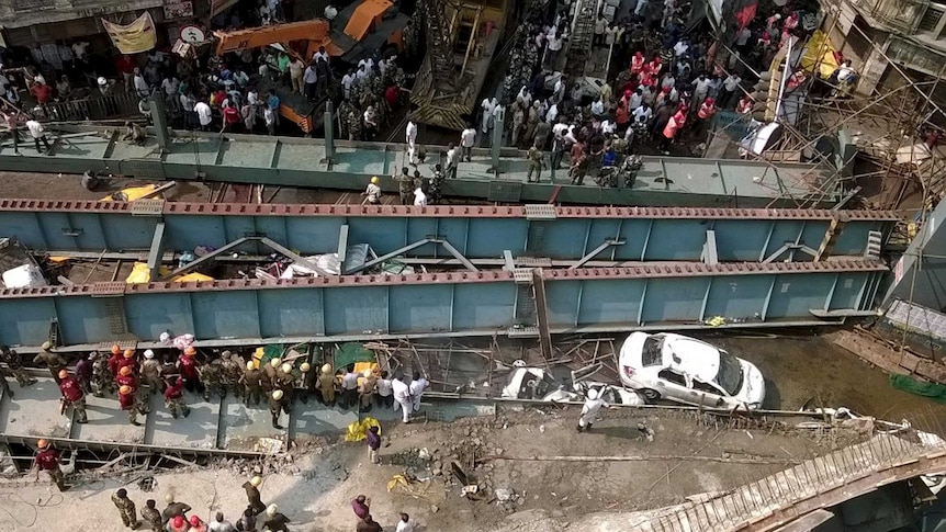 A bridge lies on the ground after a collapse, as emergency services work to free people