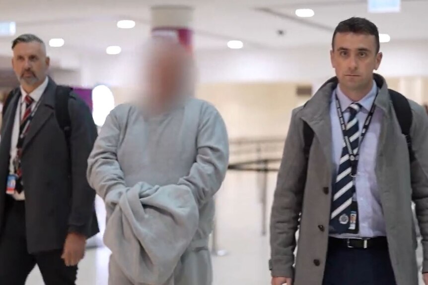 Two law enforcement officers and a man with a digitally blurred face walk through an airport.
